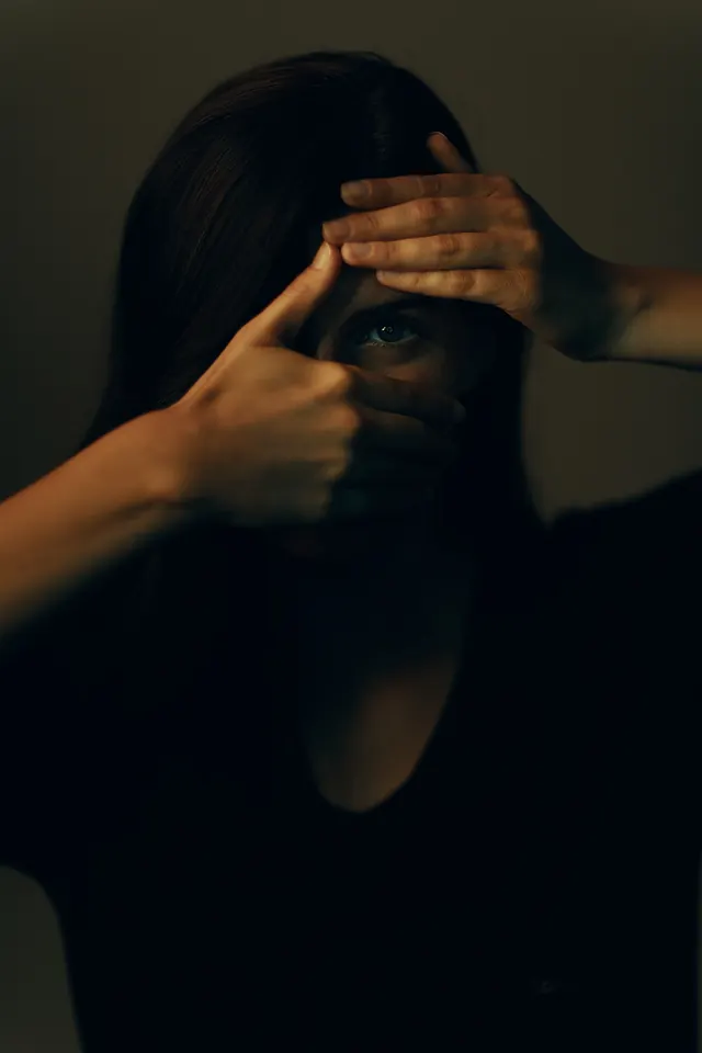 Portrait of face obscured by hands creating frame gesture, photographic, minimal, dark