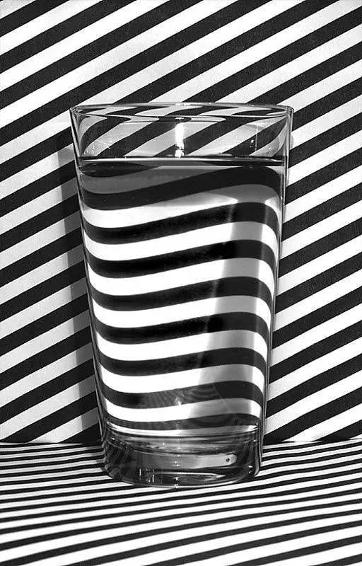 Water glass with diagonal black and white striped background pattern, photographic, geometric, monochrome