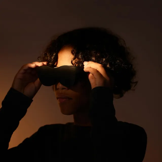 Person holding VR headset against warm-toned portrait background, photographic, minimal, dark