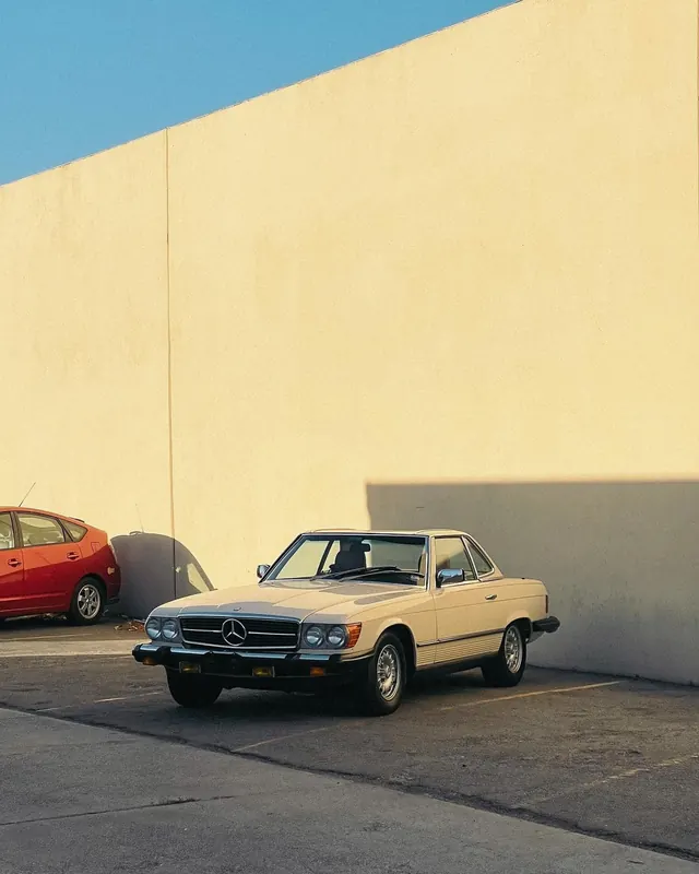 Vintage Mercedes-Benz parked against yellow wall, photographic, minimal, warm