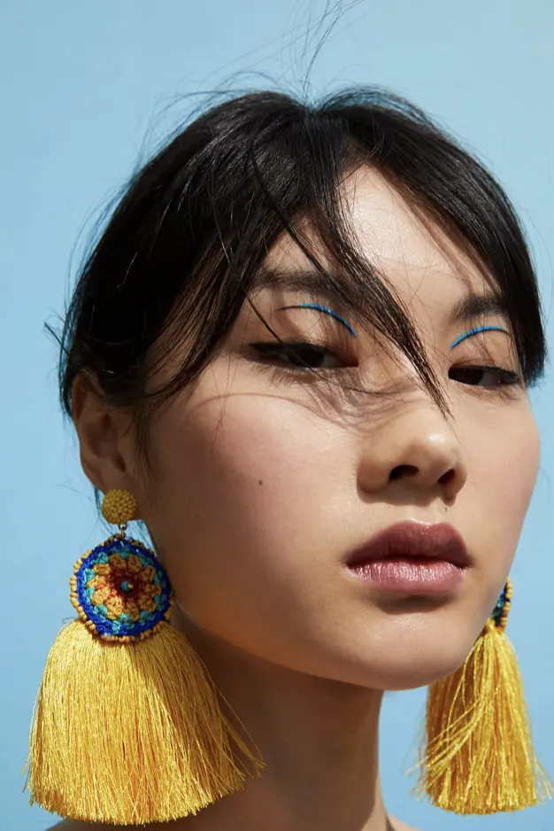 Portrait with bold yellow tassel earrings and blue eyeliner, photographic, cool