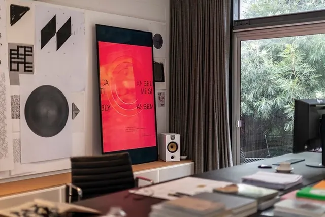 Studio desk with posters and red monitor, corporate-clean, editorial, warm