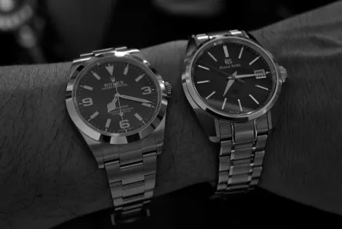 Two luxury steel watches on wrist, minimal, monochrome, dark