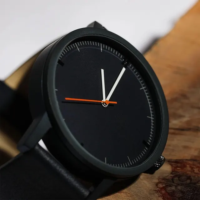 Black minimalist watch with orange accent hand on wooden surface, minimal, photographic, dark