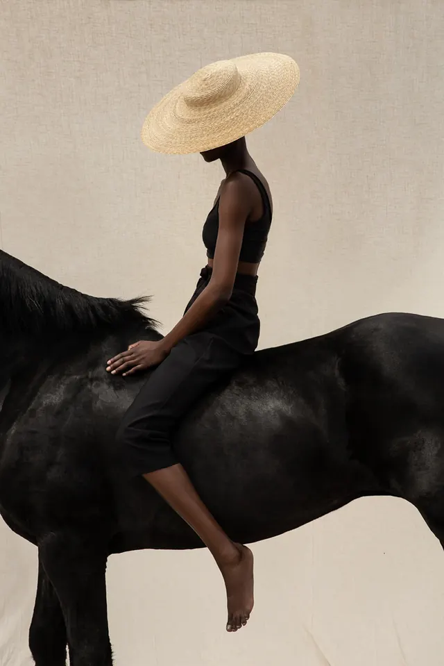 Figure in black vest on black horse with straw hat, photographic, editorial, dark