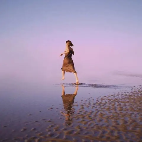 Figure in motion on wet beach at dusk, photographic, warm