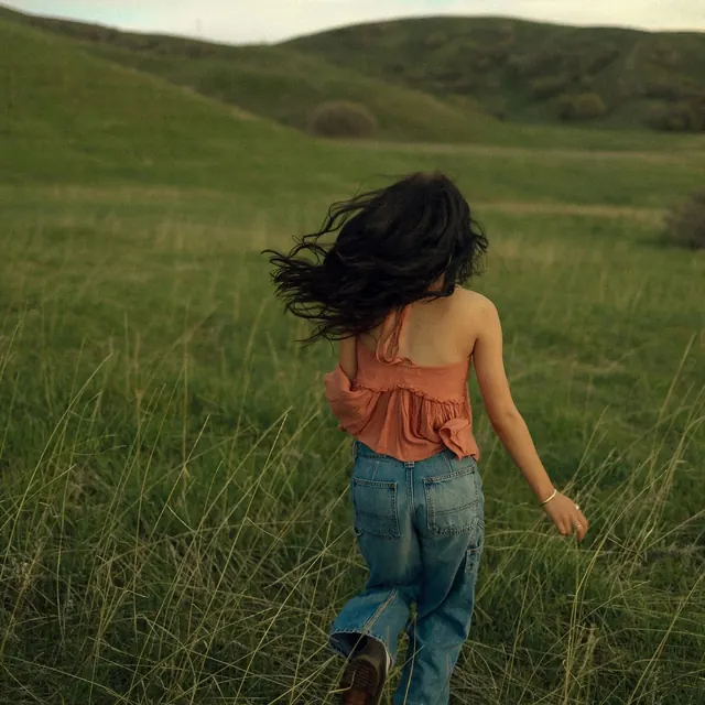 Woman walking through green field, photographic, editorial, warm